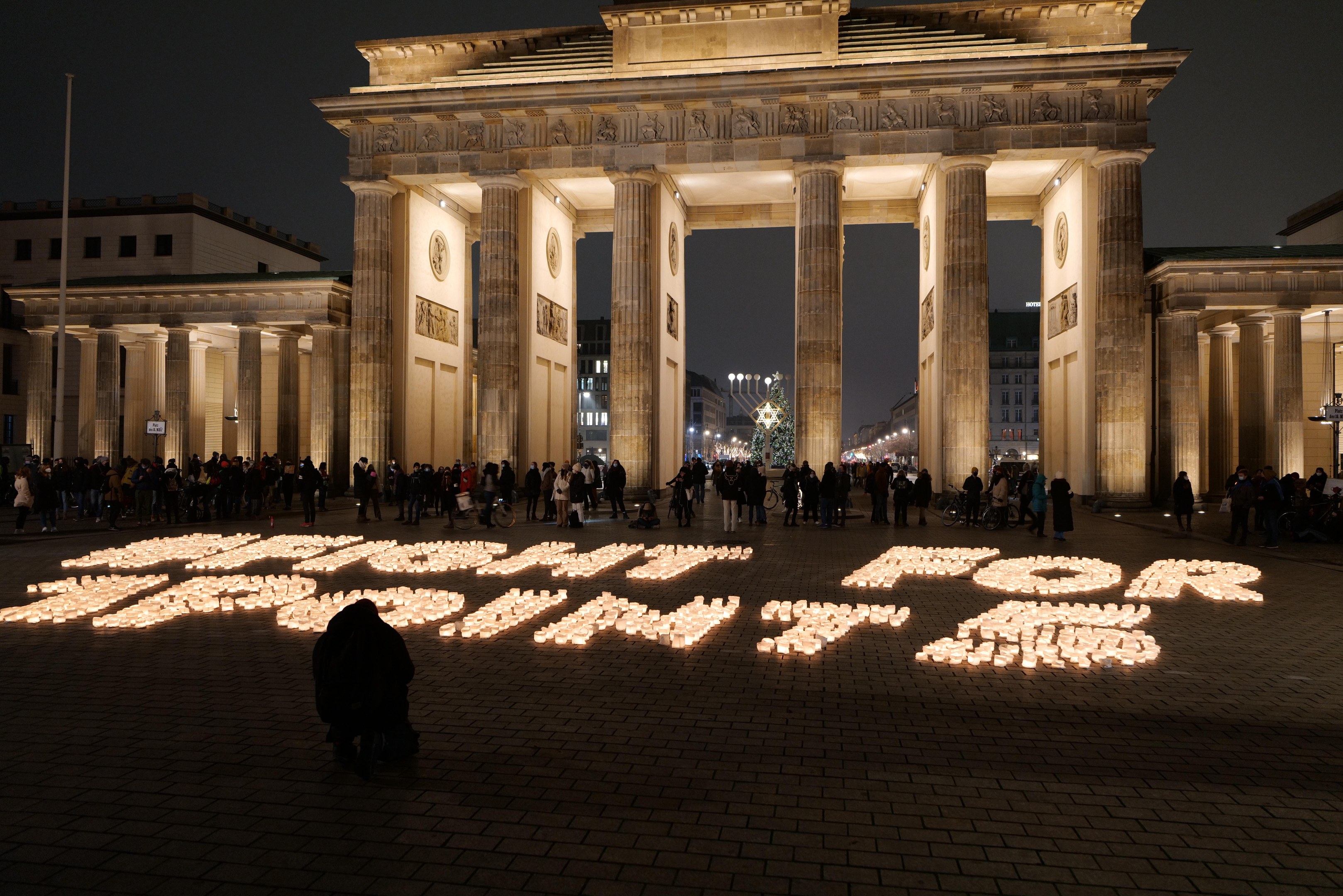 Eine Gruppe von Menschen, die vor dem beleuchteten Brandenburgertor in Berlin, Deutschland, mit 'Kampf f"ur Freiheit' auf dem Boden im Vordergrund stehen.