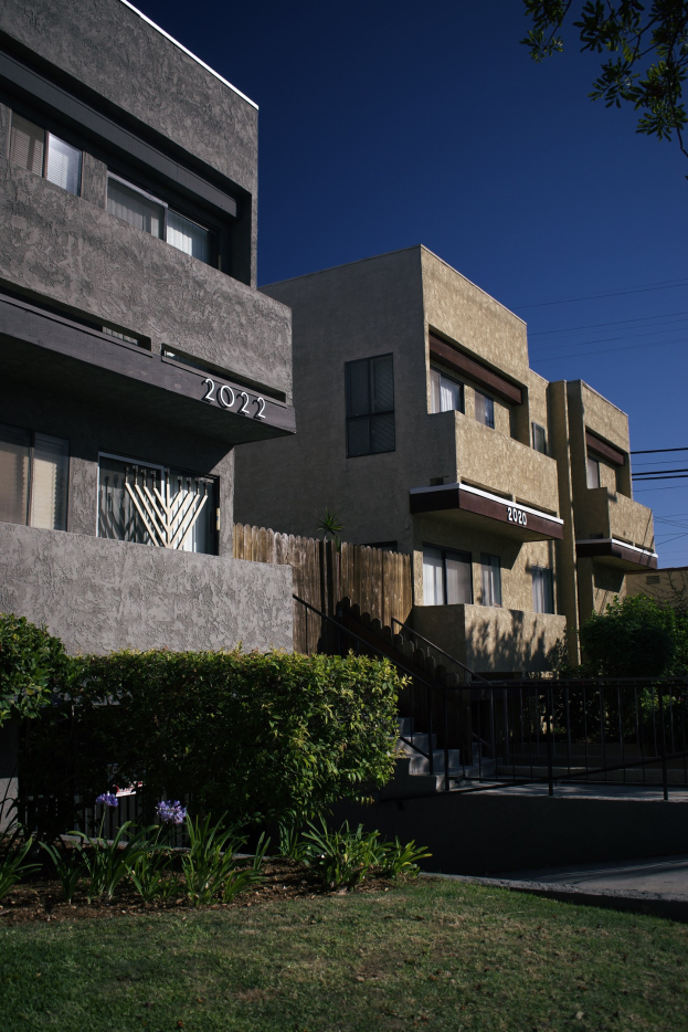 Eine Reihe von Wohngebäuden in San Francisco, Kalifornien, mit Fenstern, Pflanzen, Gras, einem Zaun, Treppen, einem Baum, Stromleitungen und einem Himmel im Hintergrund.
