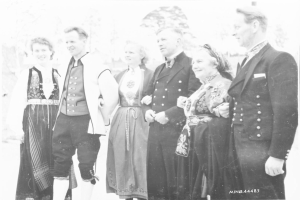 Schwarzes und wei├čes Foto einer lachenden Gruppe von Menschen, die gemeinsam überhaupt mit B├Ąumen im Hintergrund stehen, beschriftet mit "Bayerische Familie in den 1930er Jahren."