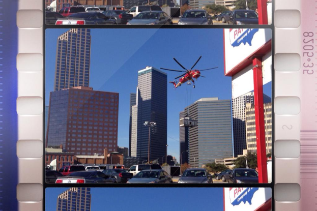 Ein Schild, das Fahrzeuge auf einer Straße, Gebäude und ein Flugzeug am Himmel zeigt.