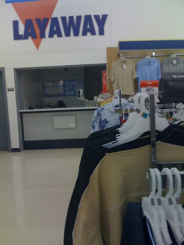 Ein Innenblick in einen Laden mit Kleidung an Bügeln, einem Tisch und einer Preisausschreibetafel.