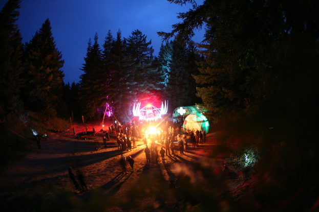 Eine Gruppe von Menschen, die eine Party in einer Hütte mit roten und grünen Scheinwerfern feiern, mit großen Bäumen im Hintergrund.