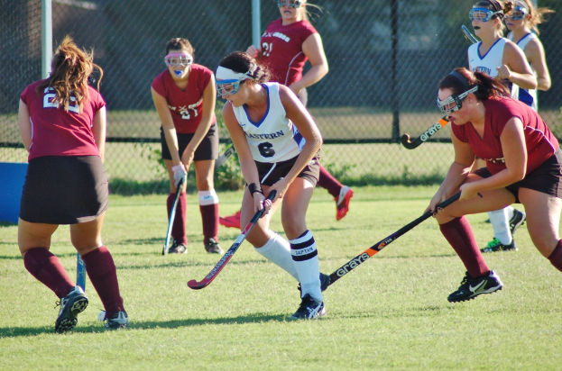 Frauen spielen Hockey auf einem Rasenfeld mit einem Netz-Hintergrund.