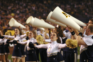 Eine Gruppe Cheerleader, die auf einem Footballfeld performen, einige halten Megafone und Pompons, mit einem unscharfen Hintergrund.