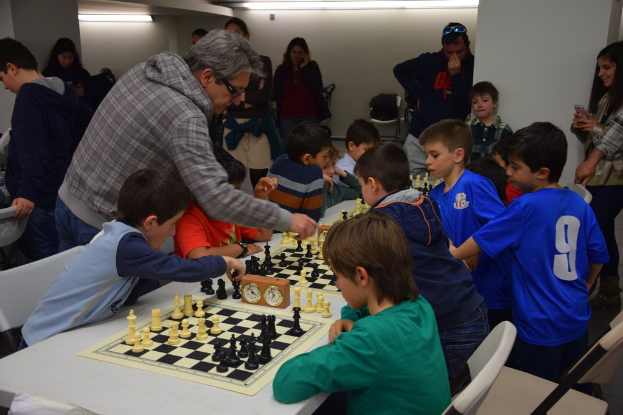 Kinder beim Schachspielen in einem Wettbewerb, mit Erwachsenen im Hintergrund.