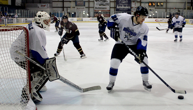 Eine Gruppe junger M├Ąnner, die auf einem Eisplatz Eishockey spielen, tragen Helme und halten Hockeyschl├Ąger, mit einem Torpfosten links und Bannern im Hintergrund.