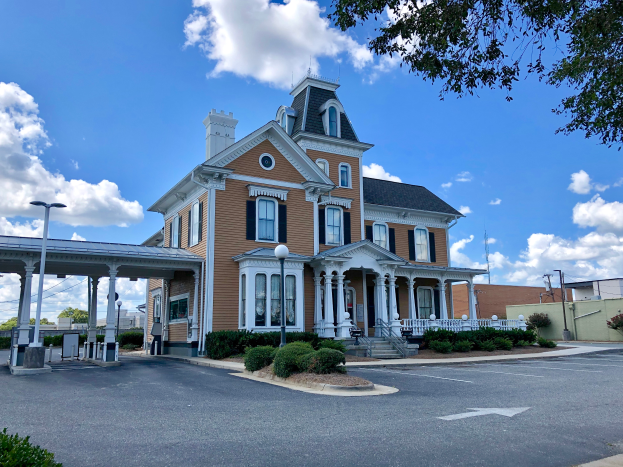 Ein großes gelbes historisches Union Station Gebäude mit einem Uhrenturm, umgeben von Straßenmasten, Straßenlaternen, Kraftfahrzeugen, Sträuchern, Bäumen und einem bewölktem Himmel.