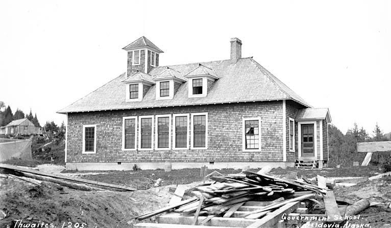 Schwarzes und weißes Foto eines Regierungsgebäudes aus dem Jahr 1905 mit Fenstern, Türen, Bäumen und einem klaren Himmel, das hölzerne Bretter und Text am unteren Rand zeigt.