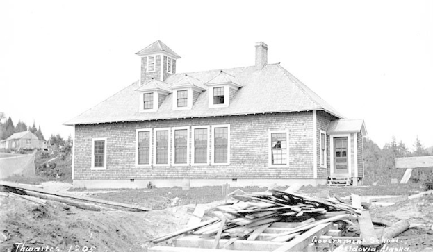 Schwarzes und weißes Foto eines Regierungsgebäudes aus dem Jahr 1905 mit Fenstern, Türen, Bäumen und einem klaren Himmel, das hölzerne Bretter und Text am unteren Rand zeigt.