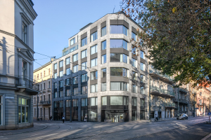 Großes Bürogebäude mit mehreren Fenstern, umgeben von Straßeninfrastruktur, Fahrzeugen, Fußgängern, Bäumen und einem bewölkten Himmel, das als neue Firmenzentrale dient.