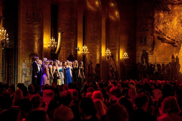 Gruppe von Menschen auf einer Bühne im Royal Opera House in London, mit beleuchteten Dekorationen und einem Publikum darunter.