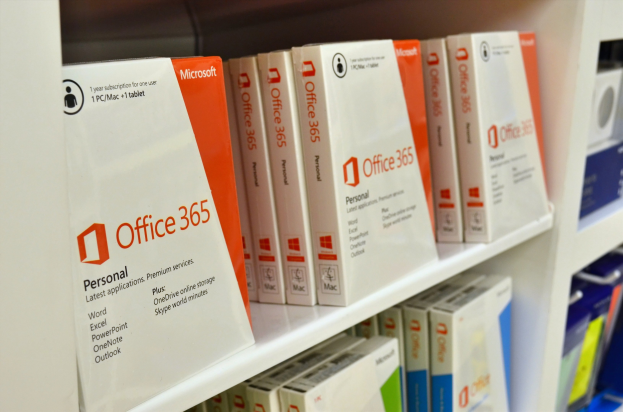 Ein weißes Regal mit ordentlich darauf angeordneten Schachteln von Microsoft Office 365, mit dem Microsoft-Logo auf der Vorderseite, vor einem leicht unscharfen Hintergrund.