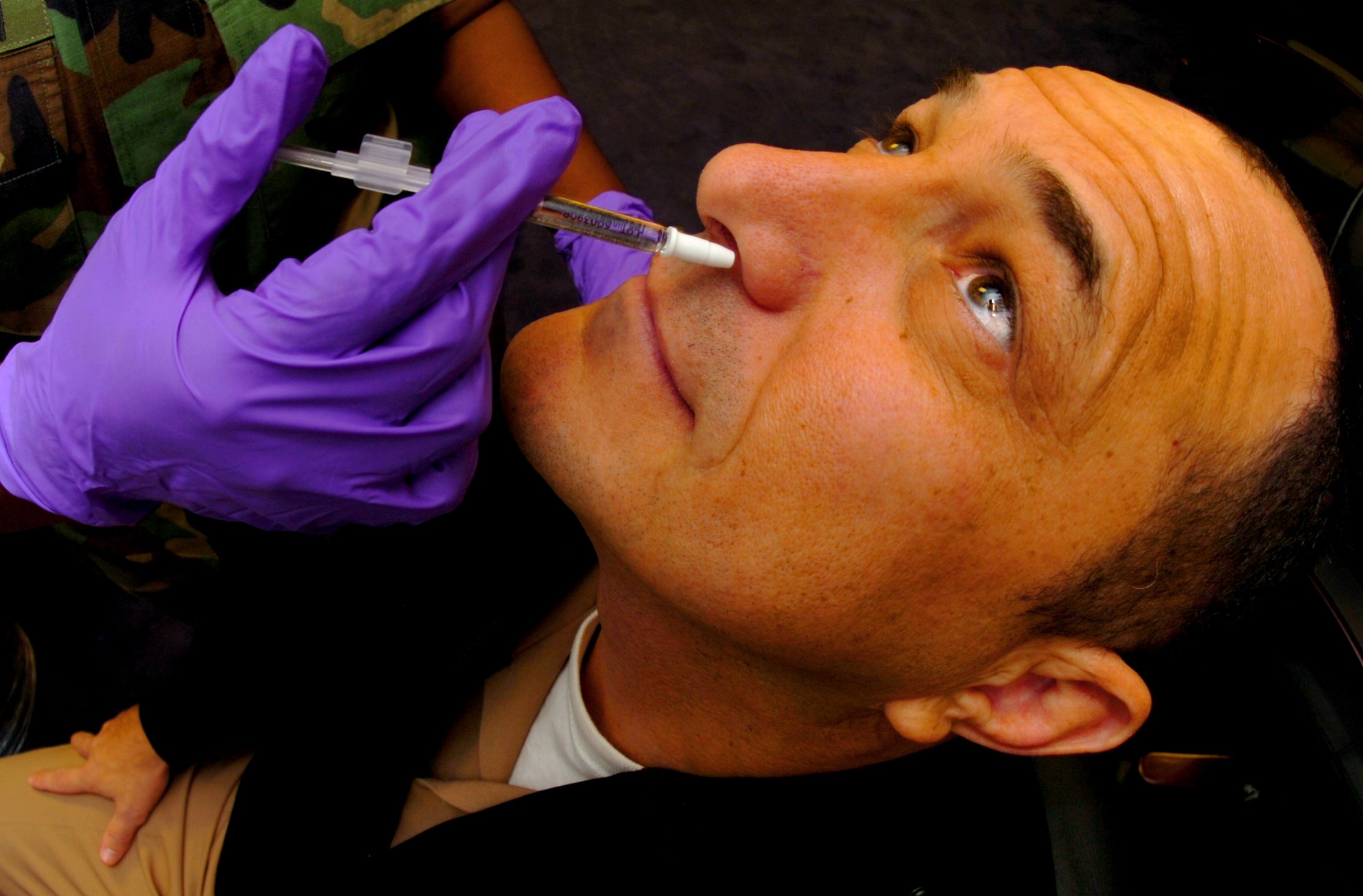 Ein Arzt in lila Handschuhen spritzt einem Mann mit einer Spritze ein Vakzin in den Mund.