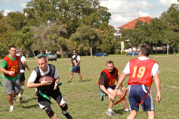Menschen, die American Football auf einem Rasenfeld mit einem Haus, Autos und Bäumen im Hintergrund spielen.