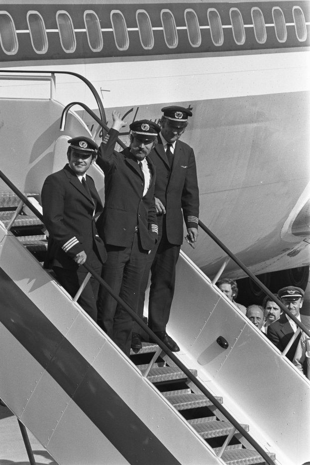Eine Gruppe von Männern in Blazern, Krawatten und Kappen, die auf einer Treppe eines Flugzeugs in einem Schwarz-Weiß-Foto stehen.