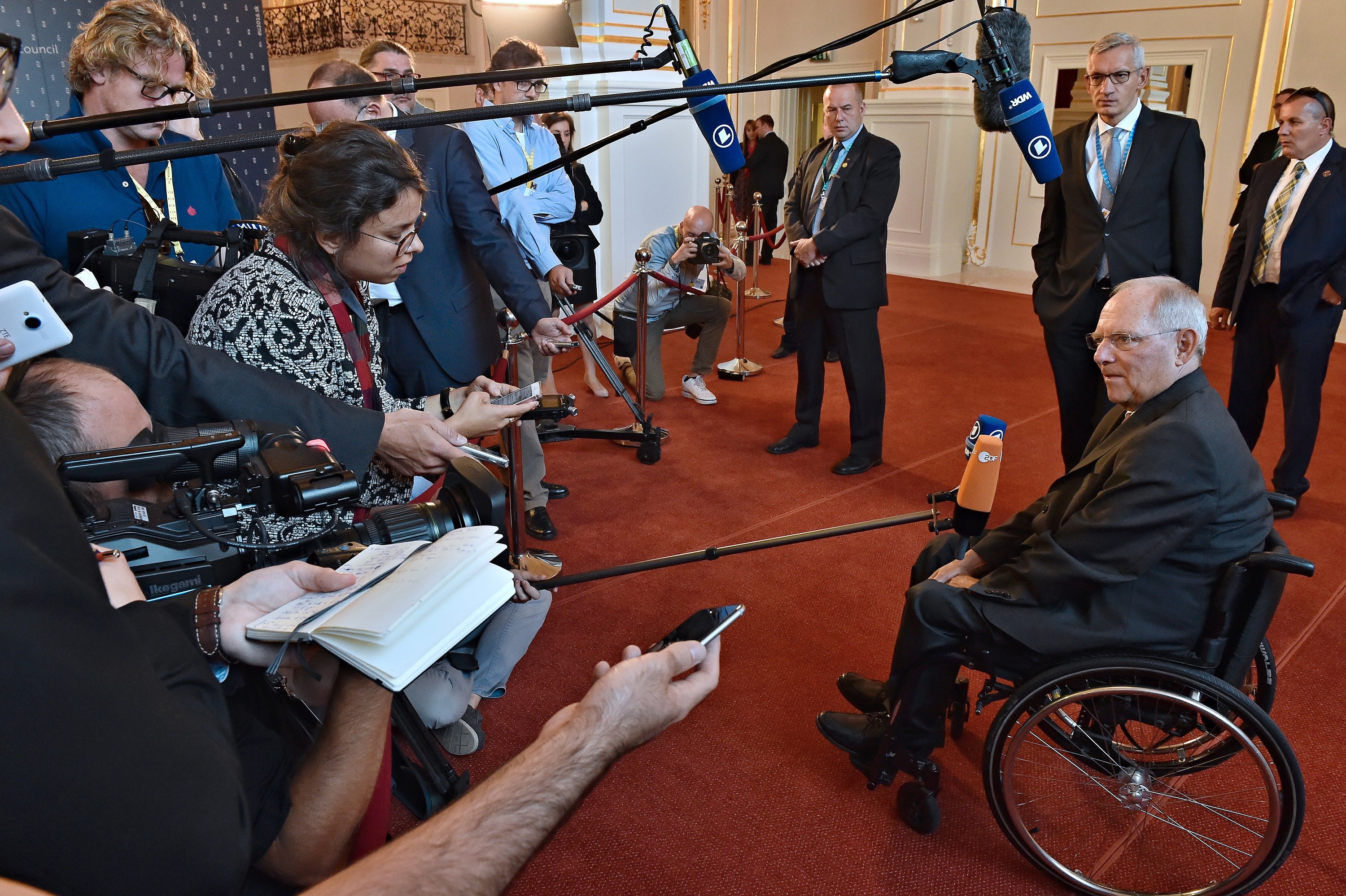 Ein Mann im Rollstuhl von Reportern mit Kameras, Mikrofonen und Handys umgeben