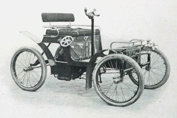 Ein Schwarz-Weiß-Foto eines frühen Elektroautos aus den 1900er-Jahren mit schlankem, aerodynamischem Design, großem runden Scheinwerfer, geschwungener Dachlinie, vier großen Rädern, prominentem Heckmotor, hellbeigem Sitzbezug und Armaturenbrett mit Knöpfen und Hebeln.