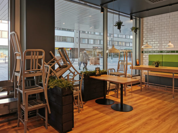 Ein Restaurantinnenraum mit Holztischen und -stühlen in der Nähe eines großen Fensters, das auf eine Straße in Berlin mit Passanten, Gebäuden und urbanen Elementen blickt.