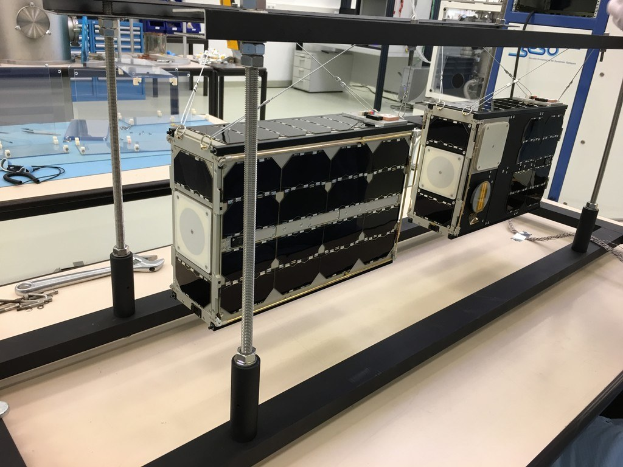 Ein Mann arbeitet an einem Satelliten in einem Labor mit NASA-Logo, umgeben von Geräten und Maschinen.