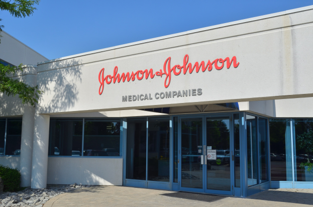 Außenansicht des Johnson & Johnson Medical Companies-Gebäudes mit Glaswänden, Text an der Fassade, Landschaftsgestaltung einschließlich Steinen und Pflanzen und einem Baum auf der linken Seite, unter einem klaren blauen Himmel.