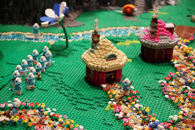 Ein Lego-Modell einer Kleinstadt mit verschiedenen Gebäuden, Pflanzen und Spielzeugen vor einem unscharfen, verträumten Hintergrund.