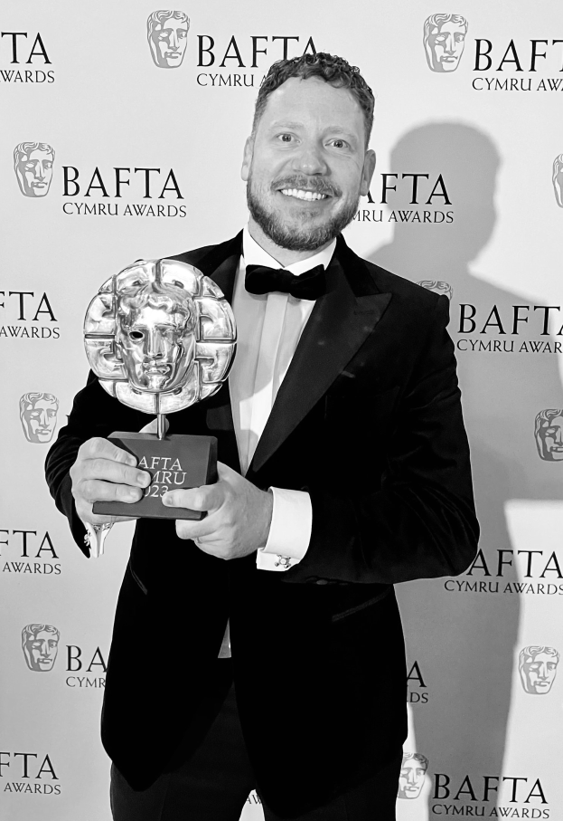 Ein Mann im Smoking lächelt, während er einen BAFTA-Award hält, mit einem "BAFTA Awards 2018"-Schild im Hintergrund.