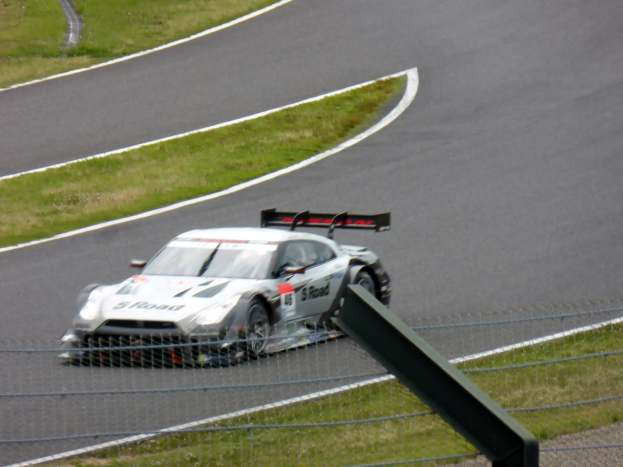 Audi R8 LMS GT3 auf der Nürburgring 24 Stunden Rennstrecke positioniert, umgeben von einem Metallzaun und grünem Gras, mit der Strecke, die sich vor ihr erstreckt.