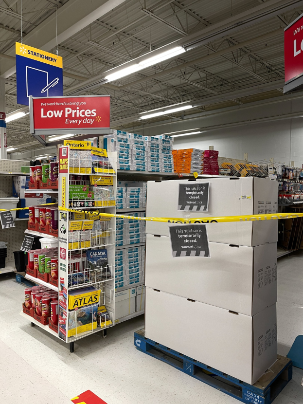 Store interior with stacked boxes, floor signs, clothing racks, informational boards, overhead lighting, and a background wall; signs indicate closure due to the coronavirus pandemic.