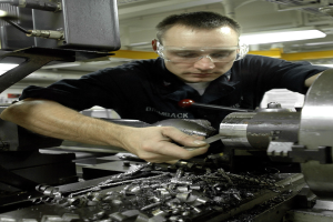 Ein Fräser mit Brille bedient eine Maschine in einer hell erleuchteten Fabrikumgebung.