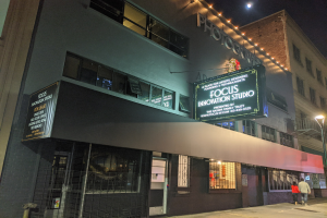 Außenansicht des Focus Innovation Studio in New York City bei Nacht, mit beleuchteten Gebäuden, Menschen auf dem Gehweg und dem Nachthimmel im Hintergrund.