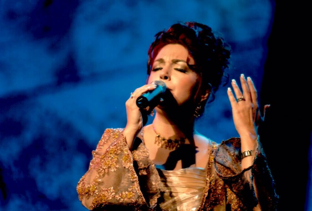 Frau in goldnem Kleid, das Mikrofon singend auf der Bühne des Eurovision Song Contest mit blauem und schwarzem Hintergrund.