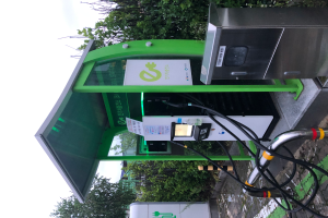 Eine Ladestation für Elektrofahrzeuge mit einem grünen und weißen Schild, umgeben von Bäumen mit einem Himmelhintergrund.