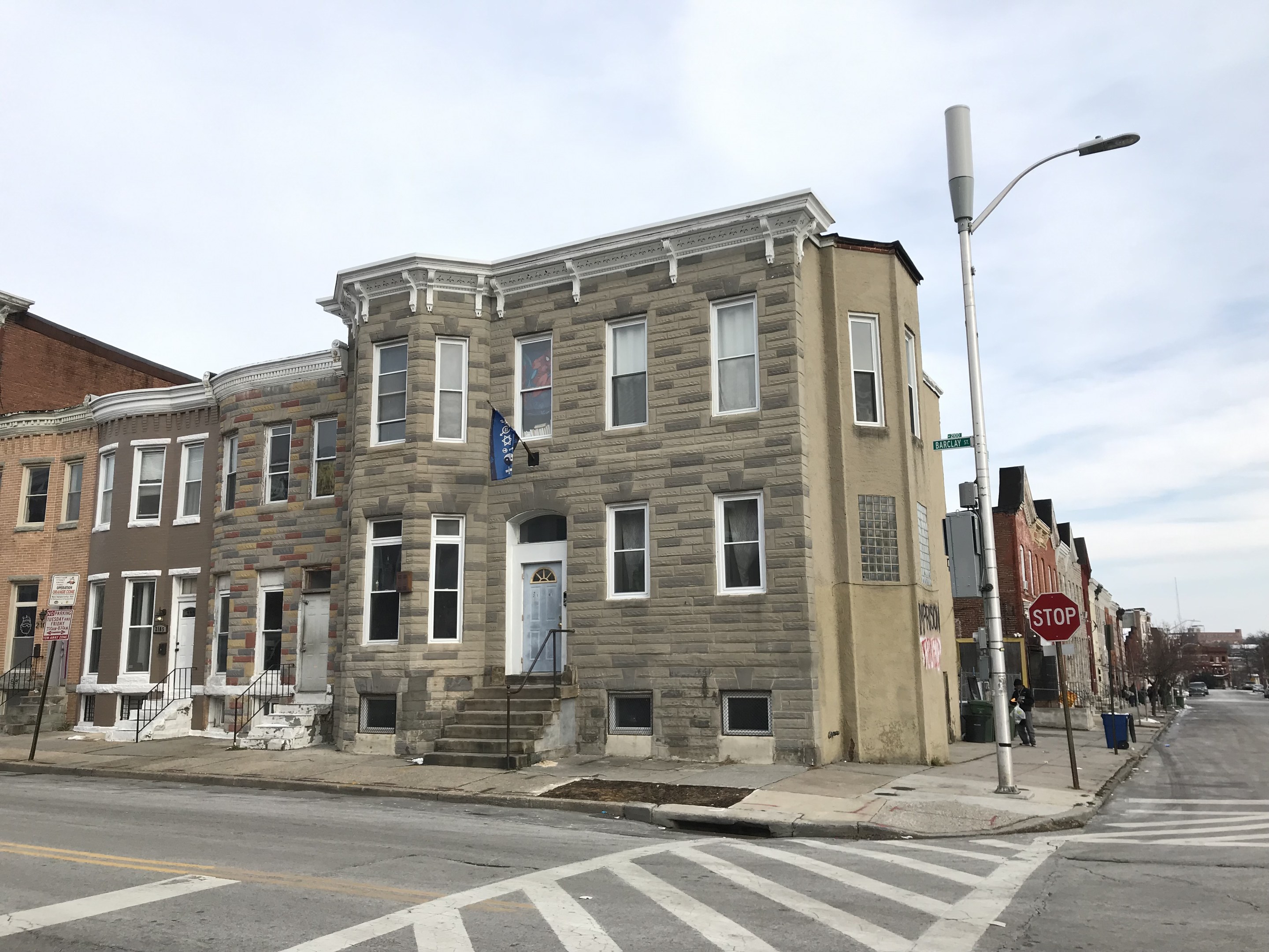 Eine Häuserreihe an einer Straßenecke in einem neuen Wohnprojekt in Philadelphia mit Fahrzeugen, Bäumen und einem bewölkten Himmel im Hintergrund.