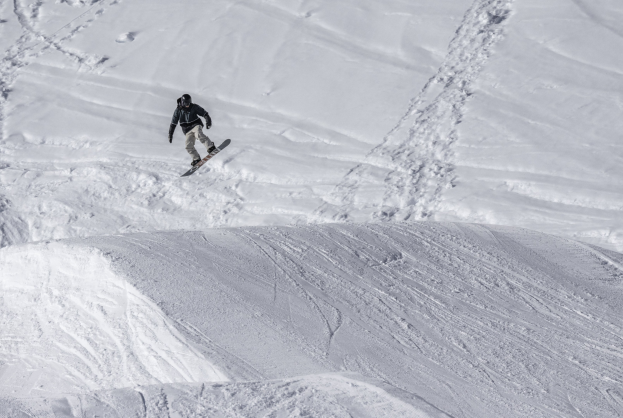 Person beim Snowboarden auf einer schneebedeckten Piste mit Helm, Handschuhen und Schuhen.