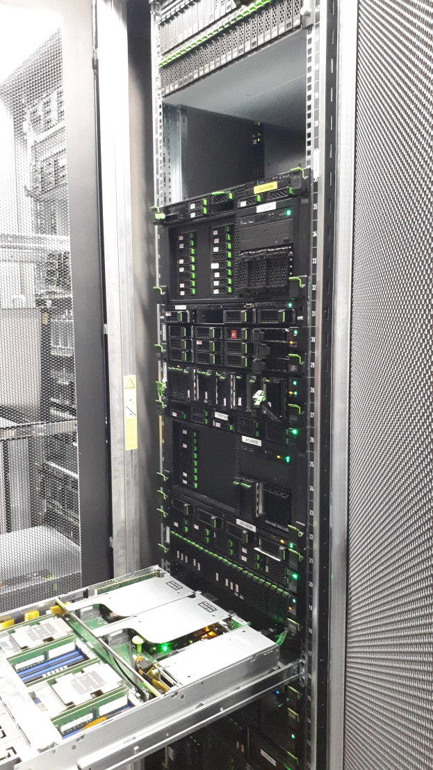 Ein Server-Rack in einem Serverraum mit Switches, Routern und anderen elektronischen Komponenten sowie einem metallischen Objekt unten und einer Decke darüber.