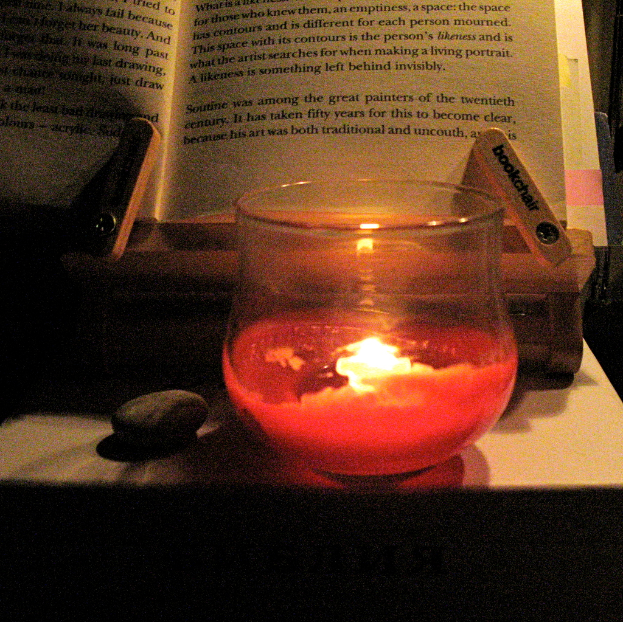 Ein Tisch mit B├╝chern, Kerzen, Gl├Ąsern, Text und einem Stein darauf.