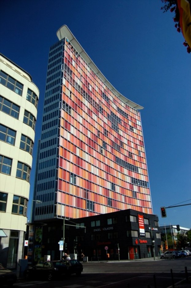 Hohe Gebäude mit geparkten Autos in einer Parkfläche und einem Verkehrszeichenmast auf der rechten unteren Seite.