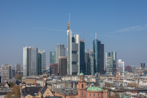 Die Skyline von Frankfurt von einem Hügel aus betrachtet, mit einem prominenten Wolkenkratzer in der Mitte und anderen Gebäuden und Bäumen im Hintergrund.