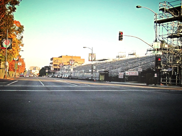 Eine Straße mit einem Verkehrsampelmast und Gerät auf der rechten Seite, Warnschilder und mehrere Fahrzeuge vor zahlreichen Bäumen auf der linken Seite.