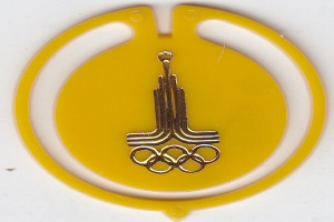 Ein gelbes Abzeichen mit den Olympischen Ringen und einem goldfarbenen Logo in der Mitte auf einem weißen Hintergrund.