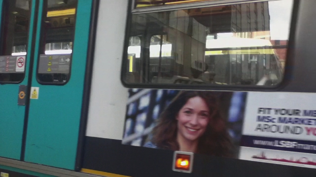 Ein Zug mit einem Tor auf der linken Seite, ein Fenster oben, das eine Brücke und einen anderen Zug zeigt, und ein Plakat unten.