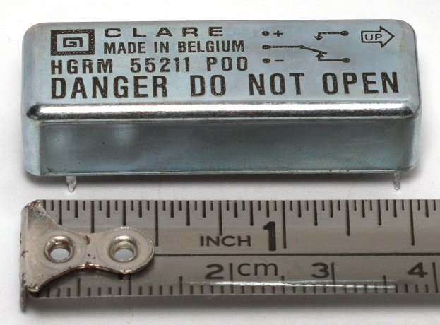 Metallbox beschriftet mit "Danger Do Not Open" neben einer Messlatte auf einer weißen Oberfläche.
