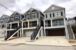 Eine Reihe von Stadthäusern in einem Wohnviertel mit einem davor geparkten Auto, umgeben von Bäumen und Drähten, unter einem bewölkten Himmel.