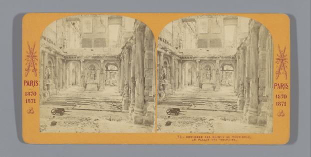 Altes Foto eines verfallenen Mehrstöckgebäudes mit zahlreichen zerbrochenen Fenstern, bröckelnden Wänden und Säulen, mit einem leeren Karren im Vordergrund.