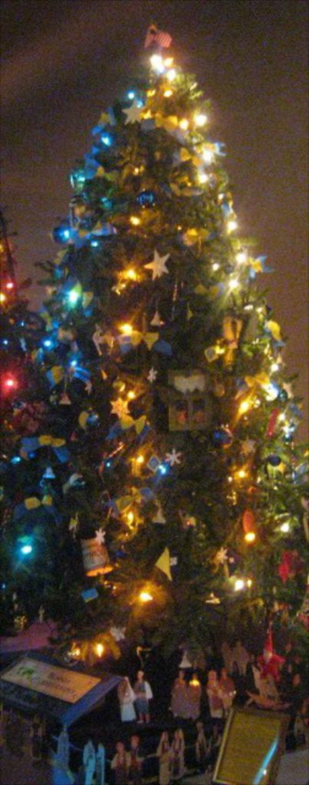 Ein geschmückter Weihnachtsbaum mit Figuren von Menschen auf einem darunter stehenden Tisch.