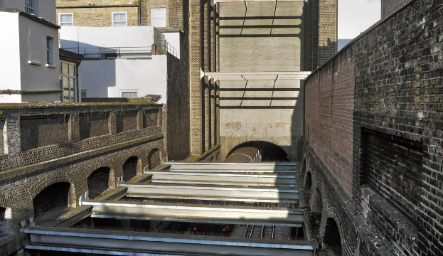 Ein Zug fährt aus einem Tunnel heraus, im Hintergrund sind Gebäude zu sehen.
