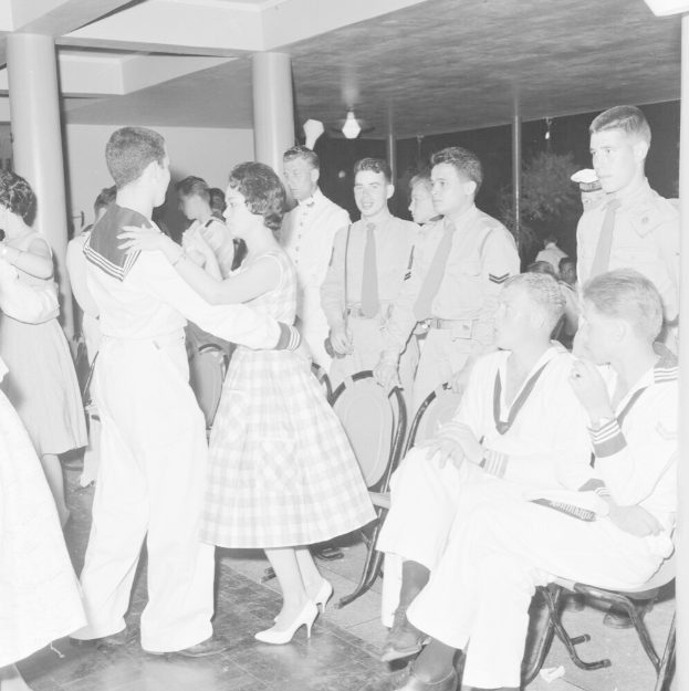 Schwarzes und weißes Bild von Militärpersonal, das auf einer Tanzfläche tanzt und sich vergnügt, mit Säulen und Lichtern im Hintergrund.