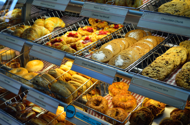 Ein Bäckereischaufenster voller verschiedener Gebäcke, Torten, Cookies und anderer Backwaren, mit Schildern, die die Art der Backwaren angeben.