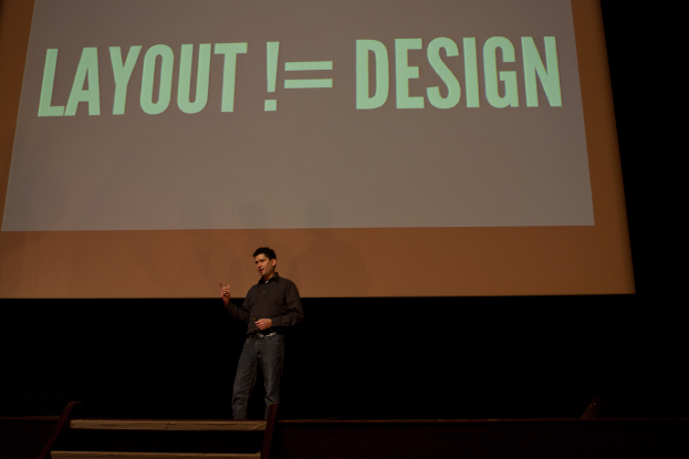 Eine Person steht auf einer Bühne und spricht, mit einem Bildschirm mit Text im Hintergrund.