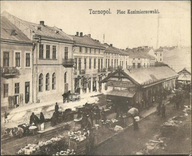 Schwarz-weiß-Foto eines belebten Marktes in Tarnopol, Polen, mit Menschen und Karren und Gebäuden im Hintergrund.